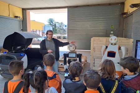 Foto de la Jornada de puertas abiertas al Instituto de Robótica e Informática Industrial (IRI, CSIC-UPC), con infantes viendo la presentación de dos robots.